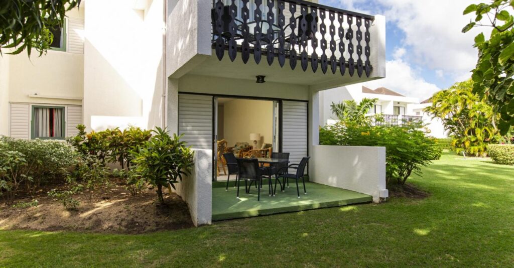 Private patio and garden outside a self-catering apartment at Plum Tree Club Barbados, with a balcony above