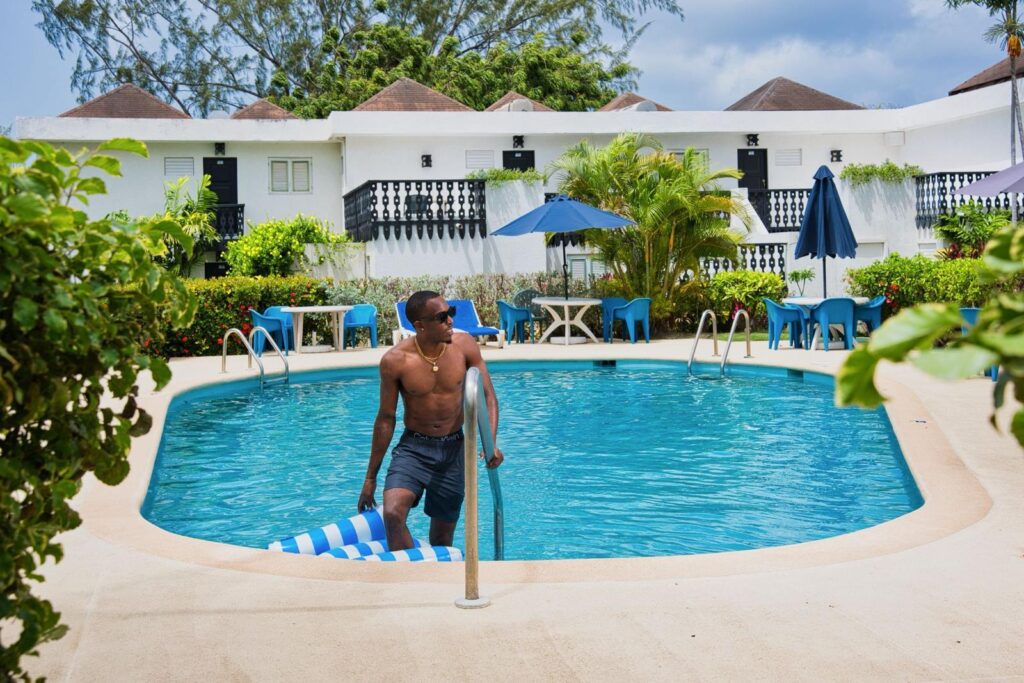 Guest stepping out of the swimming pool at Plum Tree Club Barbados, with apartment blocks, sun loungers and gardens behind